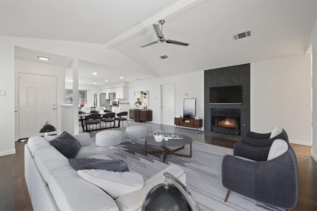 living room featuring a tile fireplace, vaulted ceiling with beams, dark hardwood / wood-style floors, and ceiling fan