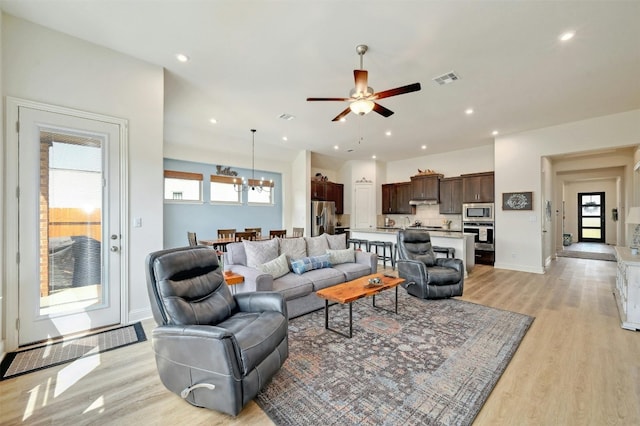 living room with a healthy amount of sunlight, light wood-type flooring, and ceiling fan with notable chandelier