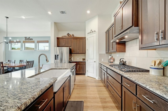 kitchen featuring light stone countertops, stainless steel appliances, an inviting chandelier, hanging light fixtures, and backsplash