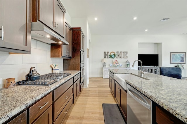 kitchen with tasteful backsplash, sink, light hardwood / wood-style flooring, light stone countertops, and stainless steel appliances