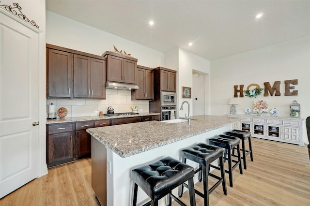 kitchen featuring stainless steel appliances, an island with sink, light hardwood / wood-style floors, sink, and a breakfast bar area