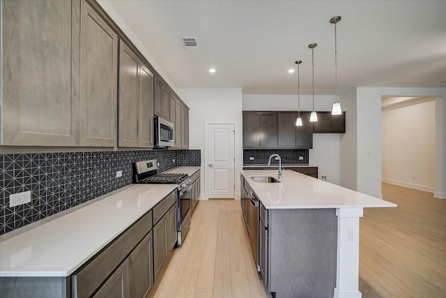 kitchen with dark brown cabinetry, sink, decorative light fixtures, a center island with sink, and appliances with stainless steel finishes