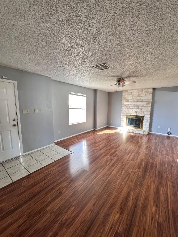 unfurnished living room with wood-type flooring, a textured ceiling, a stone fireplace, and ceiling fan