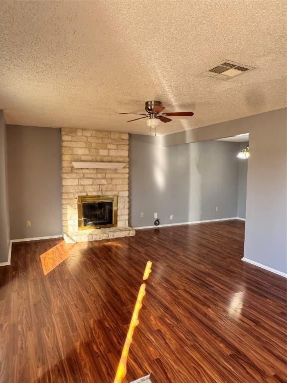 unfurnished living room with a fireplace, a textured ceiling, ceiling fan, and dark wood-type flooring