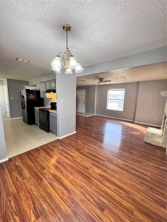 unfurnished living room featuring a textured ceiling, ceiling fan with notable chandelier, light wood-type flooring, and a fireplace