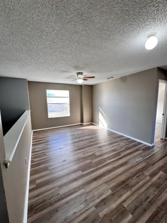 unfurnished living room featuring ceiling fan, dark wood-type flooring, and a textured ceiling