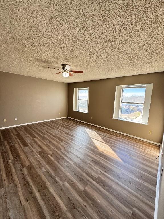 empty room featuring a textured ceiling, plenty of natural light, ceiling fan, and dark hardwood / wood-style floors