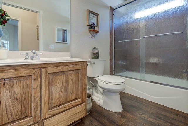 full bathroom with a wealth of natural light, combined bath / shower with glass door, toilet, vanity, and hardwood / wood-style flooring