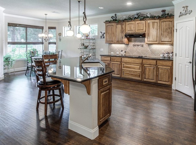 kitchen featuring pendant lighting, a kitchen island with sink, dark wood-type flooring, sink, and a kitchen bar