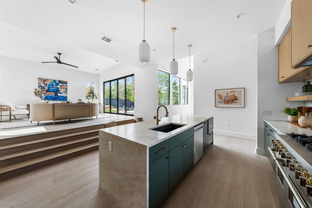 kitchen with pendant lighting, light brown cabinets, a kitchen island with sink, sink, and appliances with stainless steel finishes