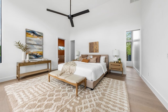 bedroom with ceiling fan, a towering ceiling, and light hardwood / wood-style flooring