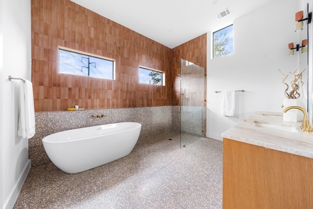 bathroom featuring vanity, a wealth of natural light, plus walk in shower, and tile walls