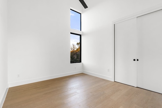 unfurnished bedroom with light wood-type flooring, high vaulted ceiling, a closet, and ceiling fan