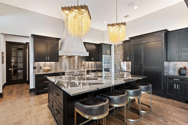 kitchen featuring light wood-type flooring, backsplash, a breakfast bar, double oven, and a center island with sink