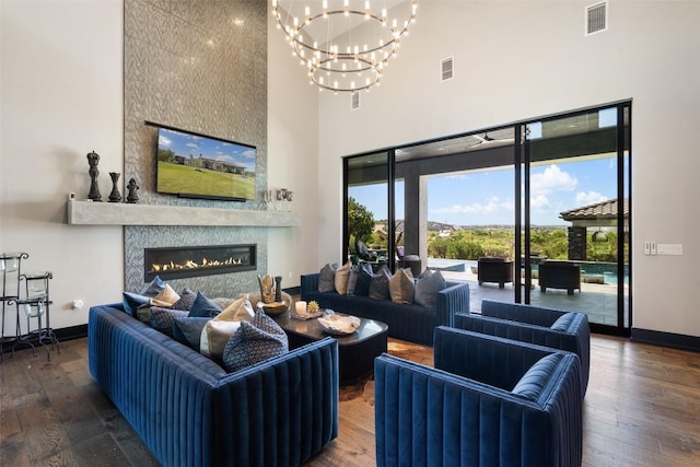 living room featuring dark hardwood / wood-style floors, a towering ceiling, a fireplace, and a chandelier