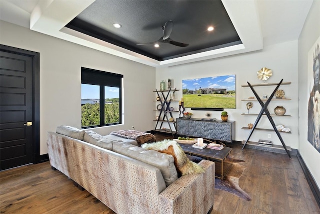 living room with a raised ceiling, ceiling fan, and dark hardwood / wood-style flooring