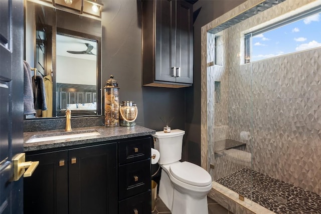 bathroom with ceiling fan, toilet, vanity, and tiled shower