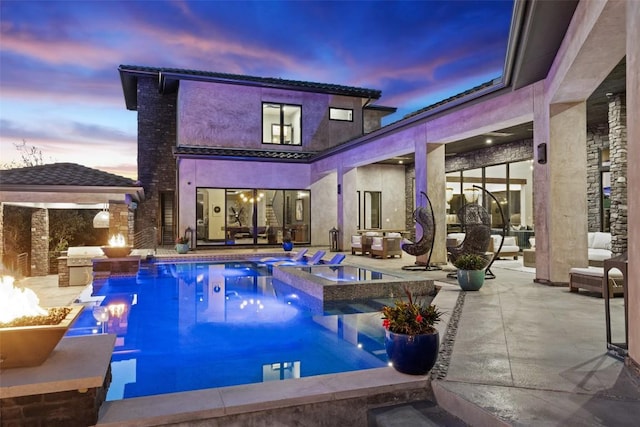 19204 Secretariat Pl, Spicewood, TX 78669 - back of house at dusk featuring an outdoor kitchen, a patio area, stucco siding, and a pool with connected hot tub