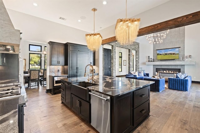 19204 Secretariat Pl, Spicewood, TX 78669 - kitchen featuring dishwasher, light wood-style flooring, tasteful backsplash, a large fireplace, and dark stone counters