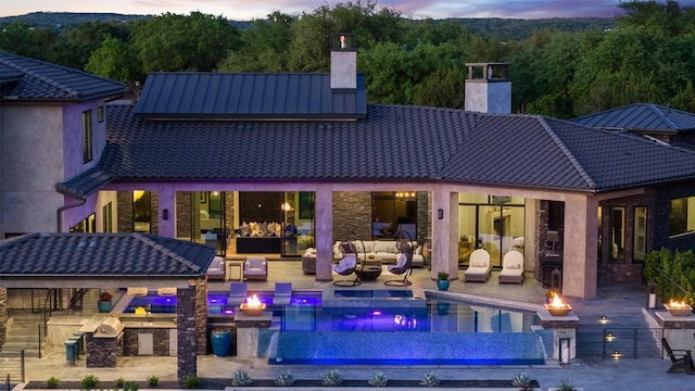 19204 Secretariat Pl, Spicewood, TX 78669 - back of property at dusk with a chimney, an outdoor living space with a fire pit, an infinity pool, a patio, and stone siding