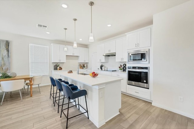 kitchen featuring appliances with stainless steel finishes, sink, pendant lighting, white cabinets, and an island with sink