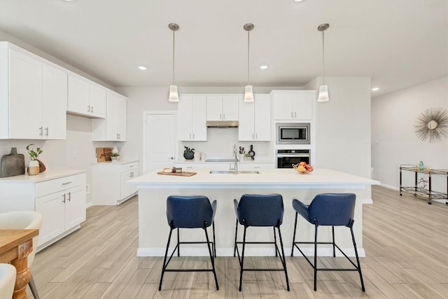 kitchen featuring appliances with stainless steel finishes, a center island with sink, white cabinetry, and decorative light fixtures