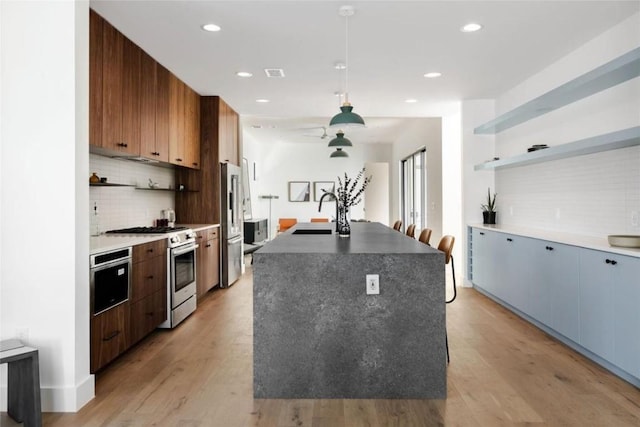 kitchen featuring sink, hanging light fixtures, premium appliances, an island with sink, and light hardwood / wood-style floors