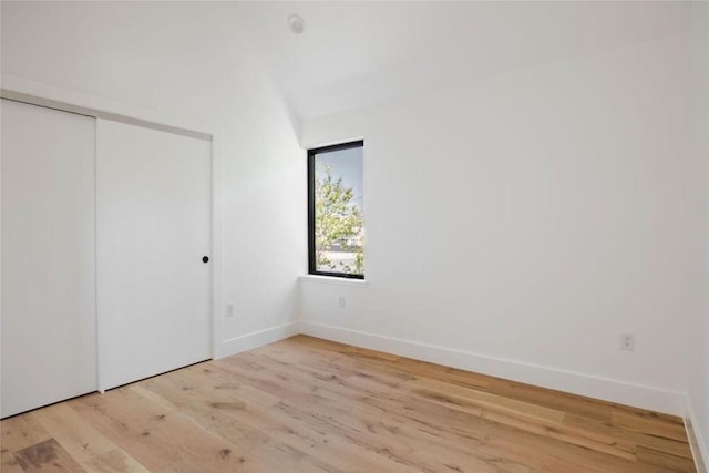 unfurnished bedroom featuring light wood-type flooring, a closet, and lofted ceiling