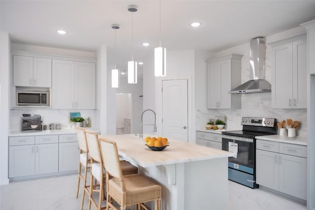 kitchen featuring hanging light fixtures, stainless steel appliances, wall chimney range hood, backsplash, and a center island with sink