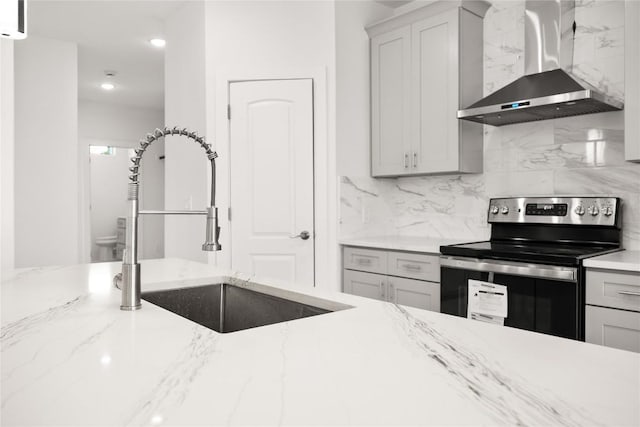 kitchen featuring sink, wall chimney range hood, tasteful backsplash, light stone counters, and stainless steel range with electric stovetop