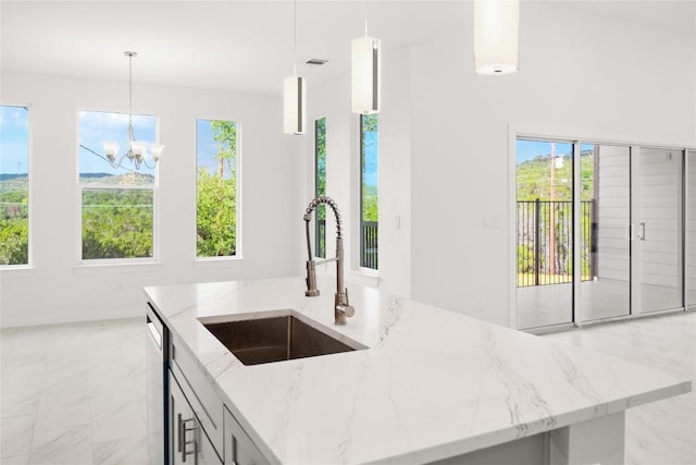 kitchen with a center island with sink, decorative light fixtures, light stone countertops, and sink