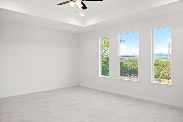 unfurnished room with ceiling fan and a tray ceiling