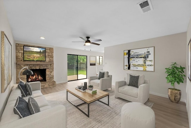 living room with a stone fireplace, ceiling fan, and light wood-type flooring