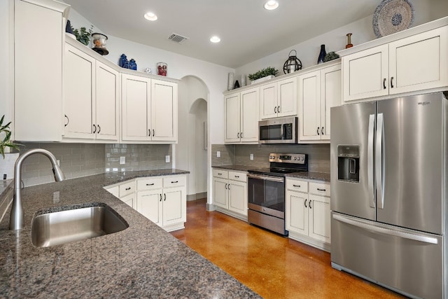 kitchen featuring arched walkways, stainless steel appliances, tasteful backsplash, a sink, and concrete floors