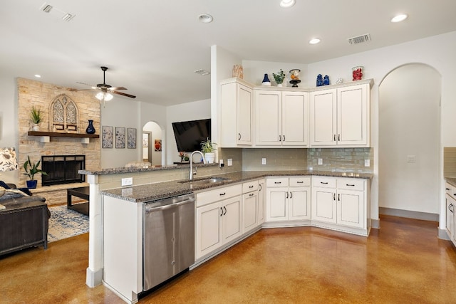 kitchen with arched walkways, open floor plan, a stone fireplace, stainless steel dishwasher, and a sink