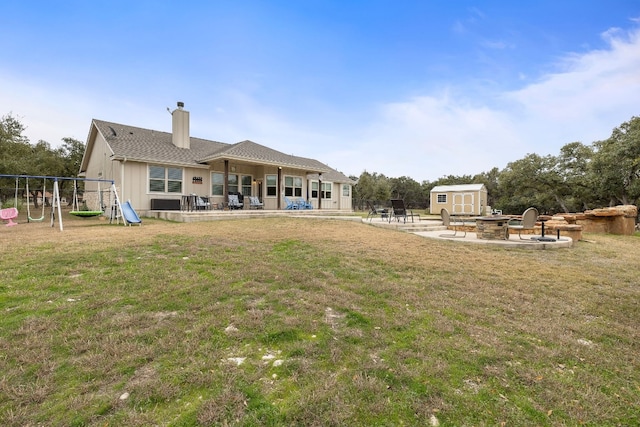 rear view of property with a playground, a fire pit, a storage shed, a yard, and a patio area