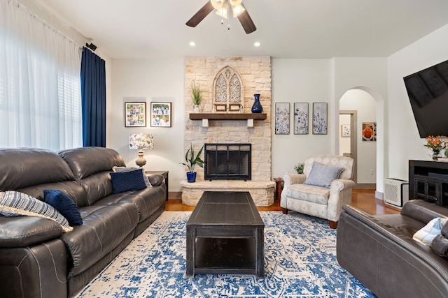 living area with a ceiling fan, a fireplace, arched walkways, and wood finished floors