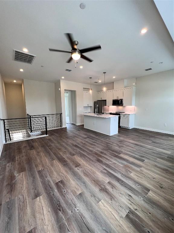 kitchen featuring dark wood-type flooring, a kitchen island with sink, black refrigerator, white cabinets, and decorative light fixtures