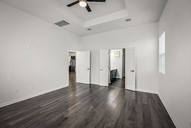 unfurnished bedroom with a towering ceiling, dark hardwood / wood-style floors, connected bathroom, ceiling fan, and a tray ceiling