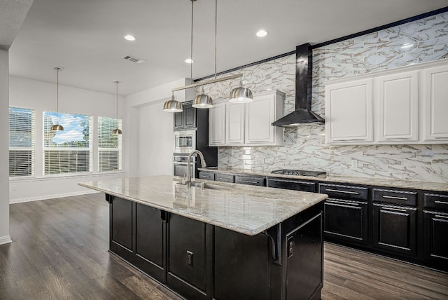 kitchen with a kitchen island with sink, sink, wall chimney range hood, and white cabinets