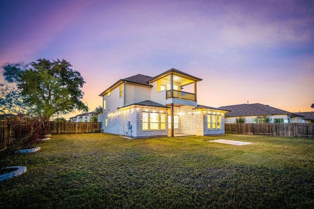 back house at dusk featuring a balcony and a yard