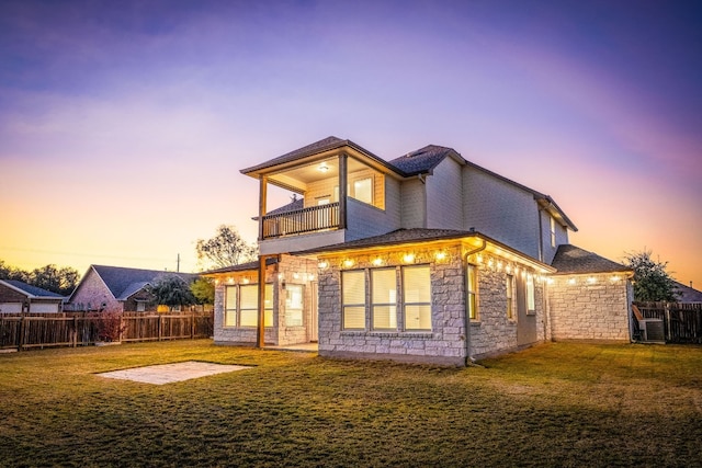 back house at dusk with central AC unit, a lawn, a patio, and a balcony