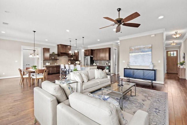 living room with ceiling fan with notable chandelier, ornamental molding, and dark wood-type flooring