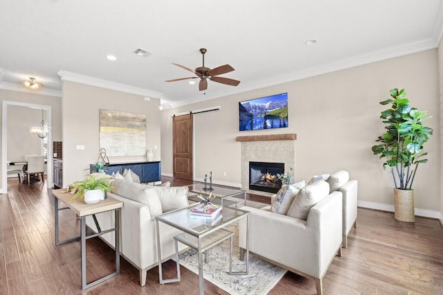 living room with ceiling fan, a barn door, wood-type flooring, and ornamental molding