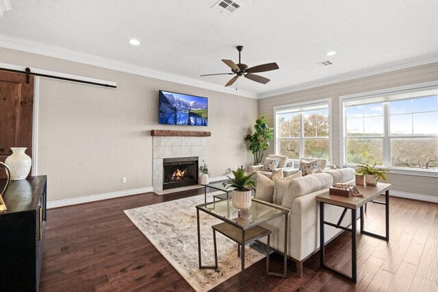 living room featuring ceiling fan, a barn door, dark hardwood / wood-style flooring, and ornamental molding