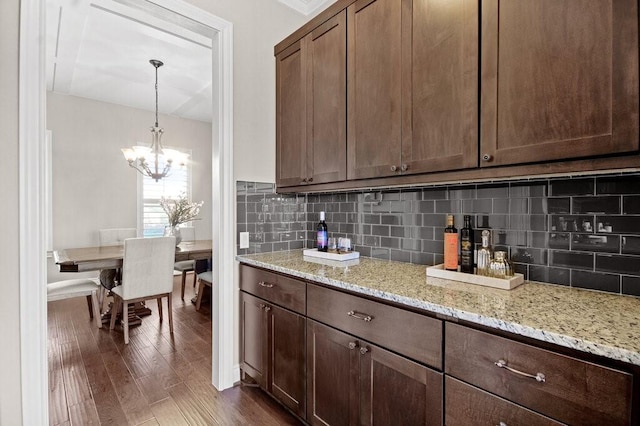 kitchen with light stone countertops, backsplash, dark brown cabinetry, dark wood-type flooring, and pendant lighting