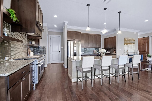 kitchen featuring hanging light fixtures, stainless steel appliances, light stone counters, a kitchen island, and a barn door