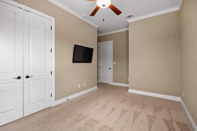 unfurnished bedroom with ceiling fan, light colored carpet, ornamental molding, and a closet