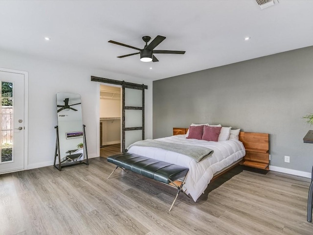 bedroom featuring ceiling fan, a barn door, a spacious closet, a closet, and light wood-type flooring