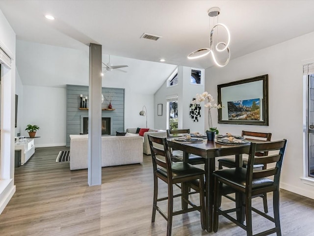 dining room featuring hardwood / wood-style flooring, ceiling fan, vaulted ceiling, and a fireplace